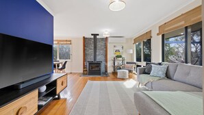 Un salon moderne doté d’un grand téléviseur à écran plat, d’une cheminée en pierre et d’un coin salon confortable avec un canapé et un pouf.