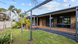 Une maison moderne dotée d’un patio couvert, de murs en pierre et de plantes tropicales.