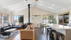 A spacious living area with a high ceiling, a fireplace, a dining area, and large windows offering views of the outdoors. - Key Lime Retreat in Cape Woolamai (Cape Woolamai)
