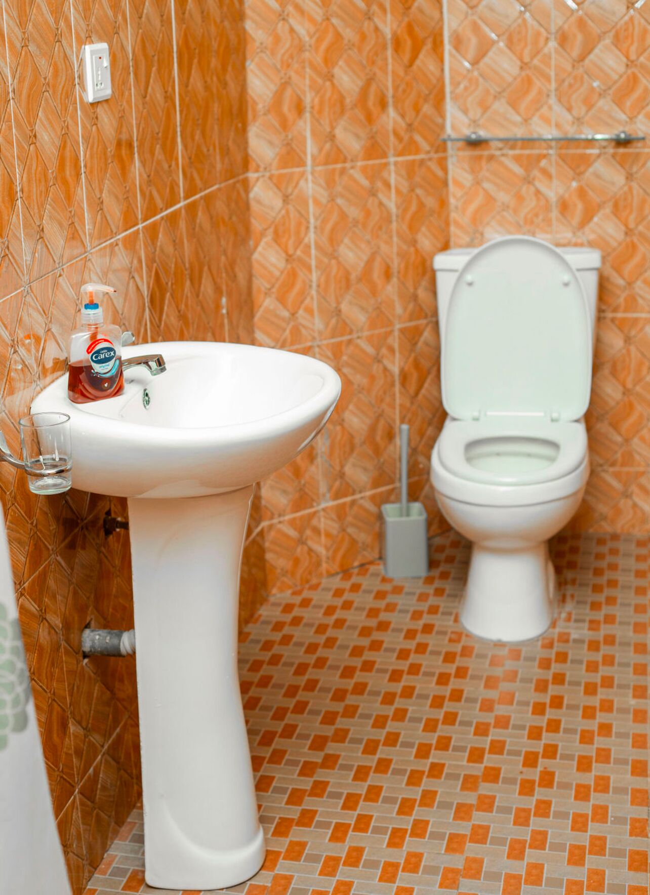 Um banheiro com pia branca, vaso sanitário e azulejos com padrão laranja.