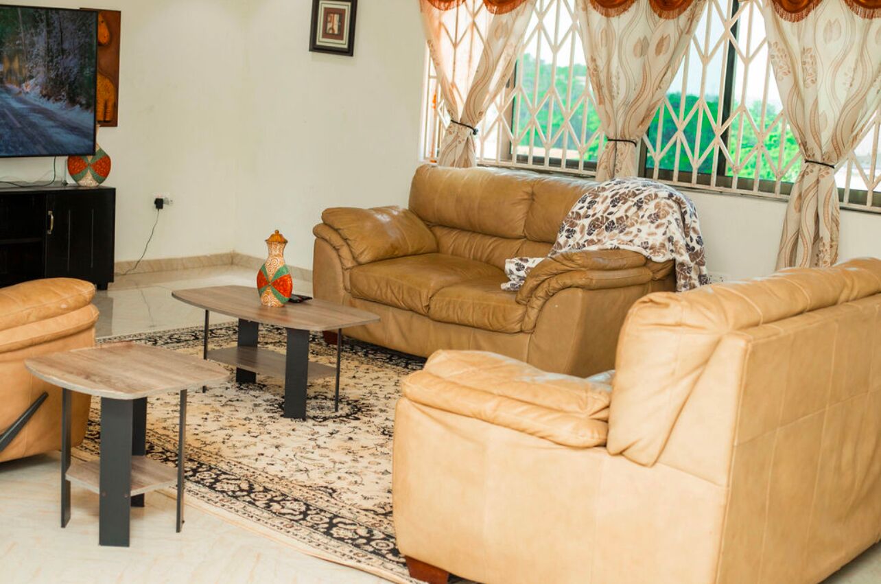 Una sala de estar con sofá, mesa de centro, reposapiés y televisor sobre un mueble.