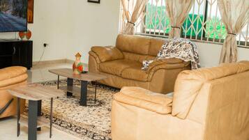 Una sala de estar con sofá, mesa de centro, reposapiés y televisor sobre un mueble.