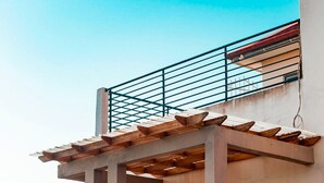 Een modern huis met een overdekte patio, een trap naar de ingang en een eethoek met stoelen en een tafel.