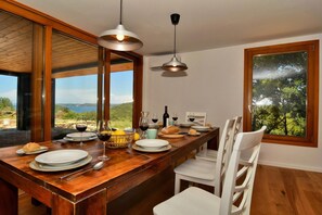 Comedor con mesa de madera dispuesta para cuatro, vista al exterior e iluminación colgante.