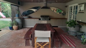 A covered patio with a wooden table and benches, a grill, and surfboards mounted on the wall. - Dunsborough Family Fun House! Walking distance to beach and town. (Dunsborough)