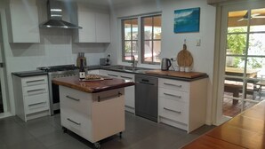 A modern kitchen with a central island, white cabinetry, stainless steel appliances, and a view to the outside. - Dunsborough Family Fun House! Walking distance to beach and town. (Dunsborough)