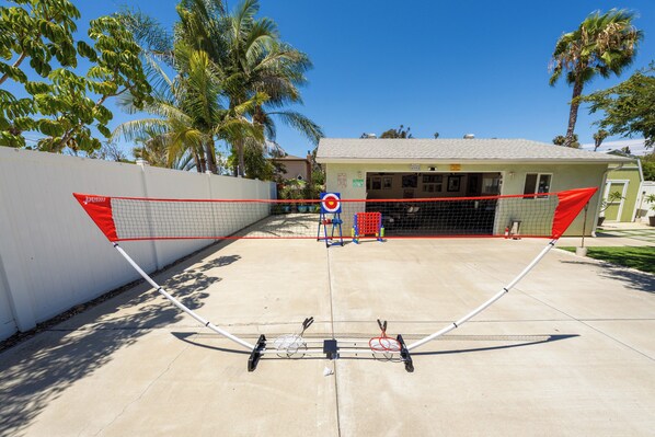 A tennis court with a net, palm trees, and a building in the background.