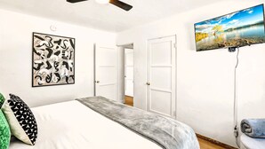 A bedroom with a bed, a ceiling fan, a TV, and a framed artwork on the wall.