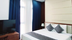 Una habitación de hotel con cama, escritorio, televisión, ventilador de techo y ventana con cortinas.