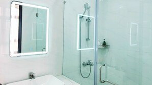 Un baño moderno con ducha envuelta en cristal, un lavabo blanco con encimera de mármol y un espejo con marco iluminado.