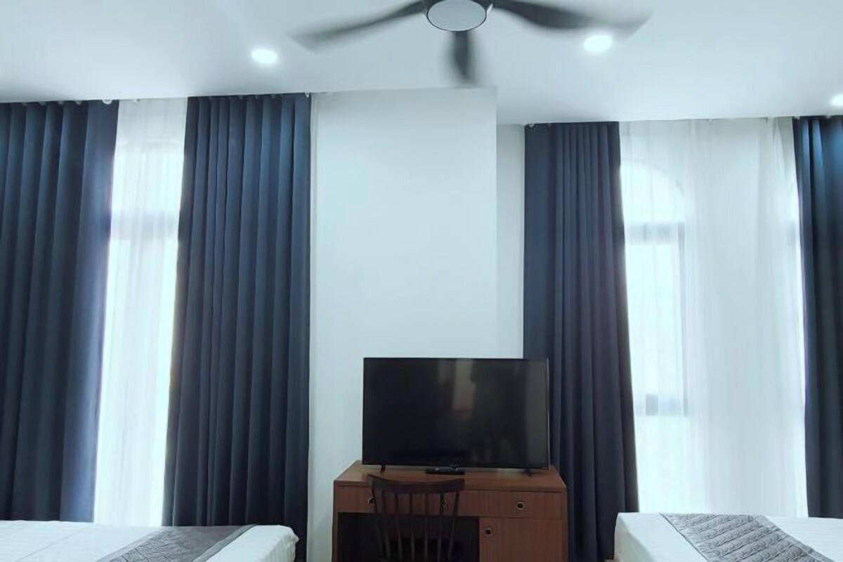 A hotel room with a bed, a desk with a television, and curtains.