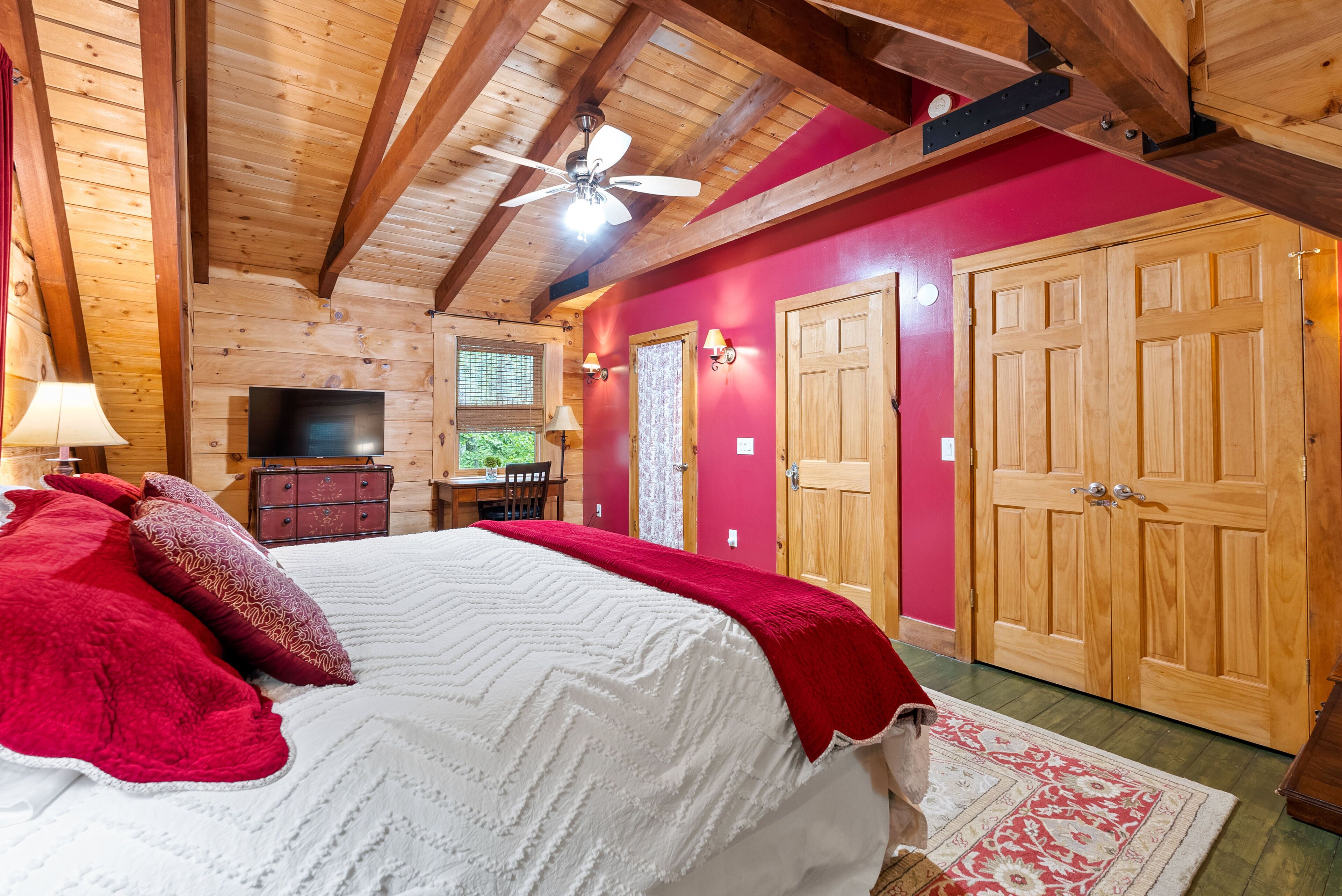Un dormitorio de cabaña de madera con una cama, paredes rojas y un ventilador de techo.