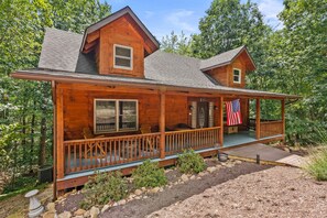 A wooden cabin with a porch, a flag, and a small deck area.