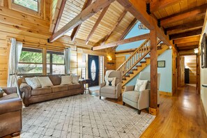 A log cabin interior with a wooden staircase, a sofa set, and a patterned rug.