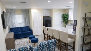 Un salon moderne avec un canapé bleu, un coin repas comprenant une table et des chaises, et une cuisine équipée d’un réfrigérateur et de placards.