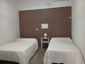 Une chambre d’hôtel avec deux lits simples, une petite table de chevet avec une lampe et un climatiseur fixé au mur.