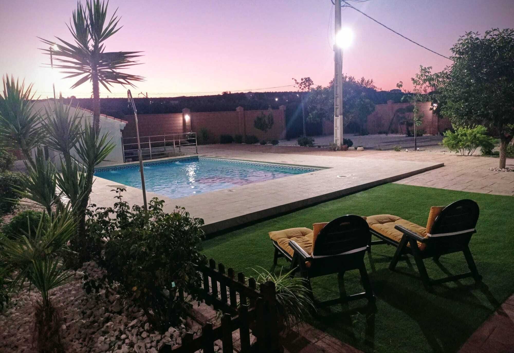 Una piscina rectangular con una terraza de madera y una pequeña mesa con dos sillas.
