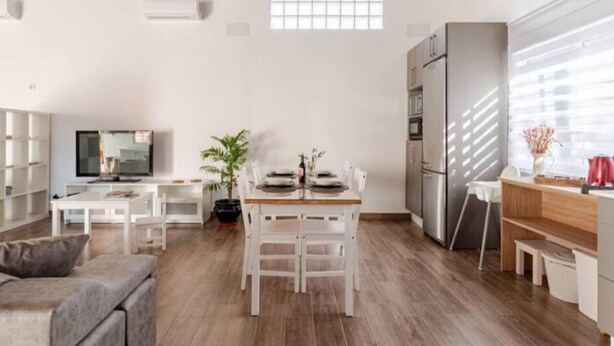 A modern kitchen with white cabinetry, a dining table with chairs, and a built-in oven. - Rincón Andaluz, Huerta Alegría (Casariche)