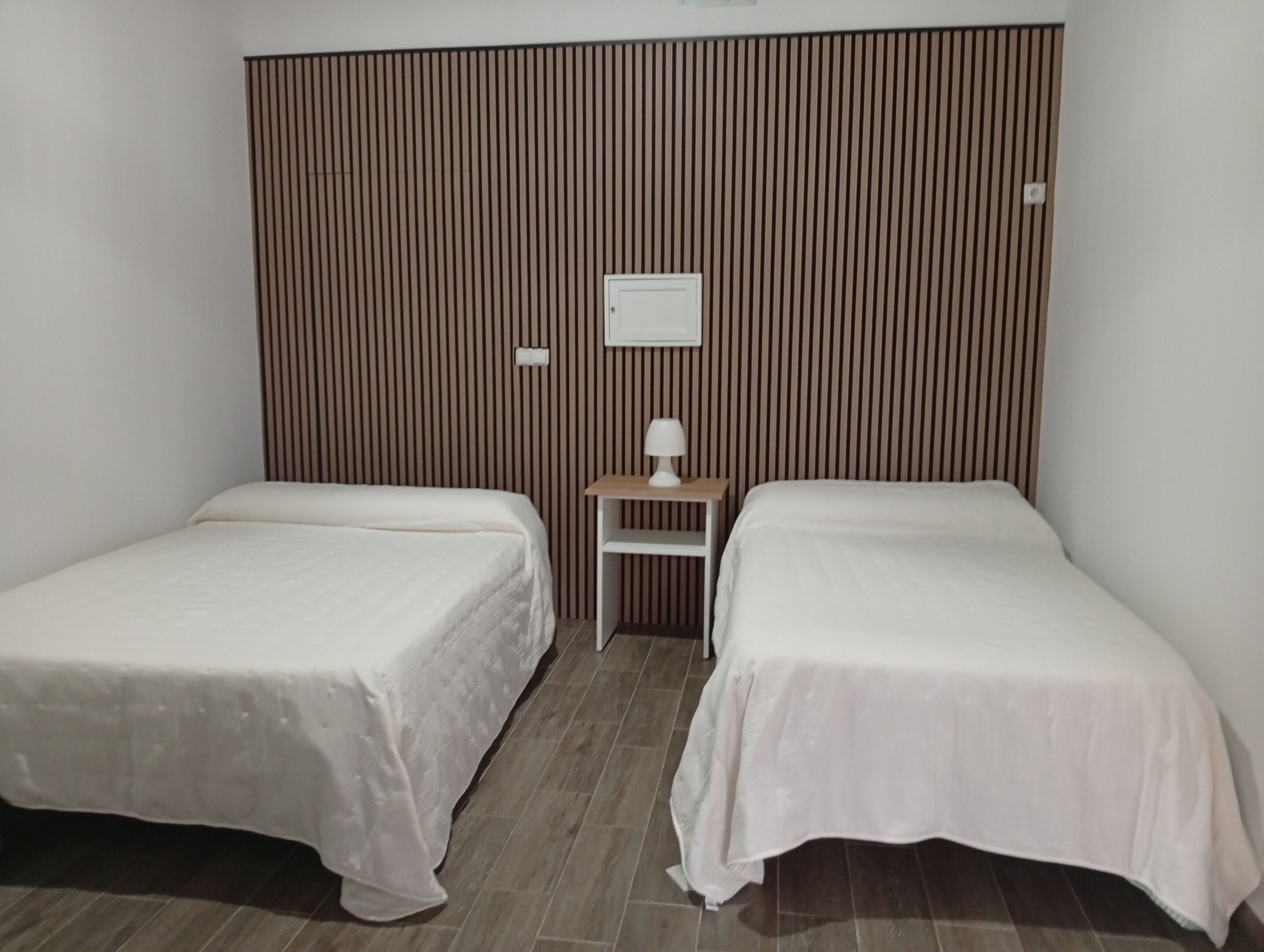 Une chambre avec deux lits simples, une petite table avec une lampe et un interrupteur fixé au mur.