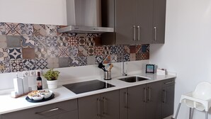 A modern kitchen with a tiled backsplash, stainless steel range hood, and grey cabinets. - Rincón Andaluz, Huerta Alegría (Casariche)