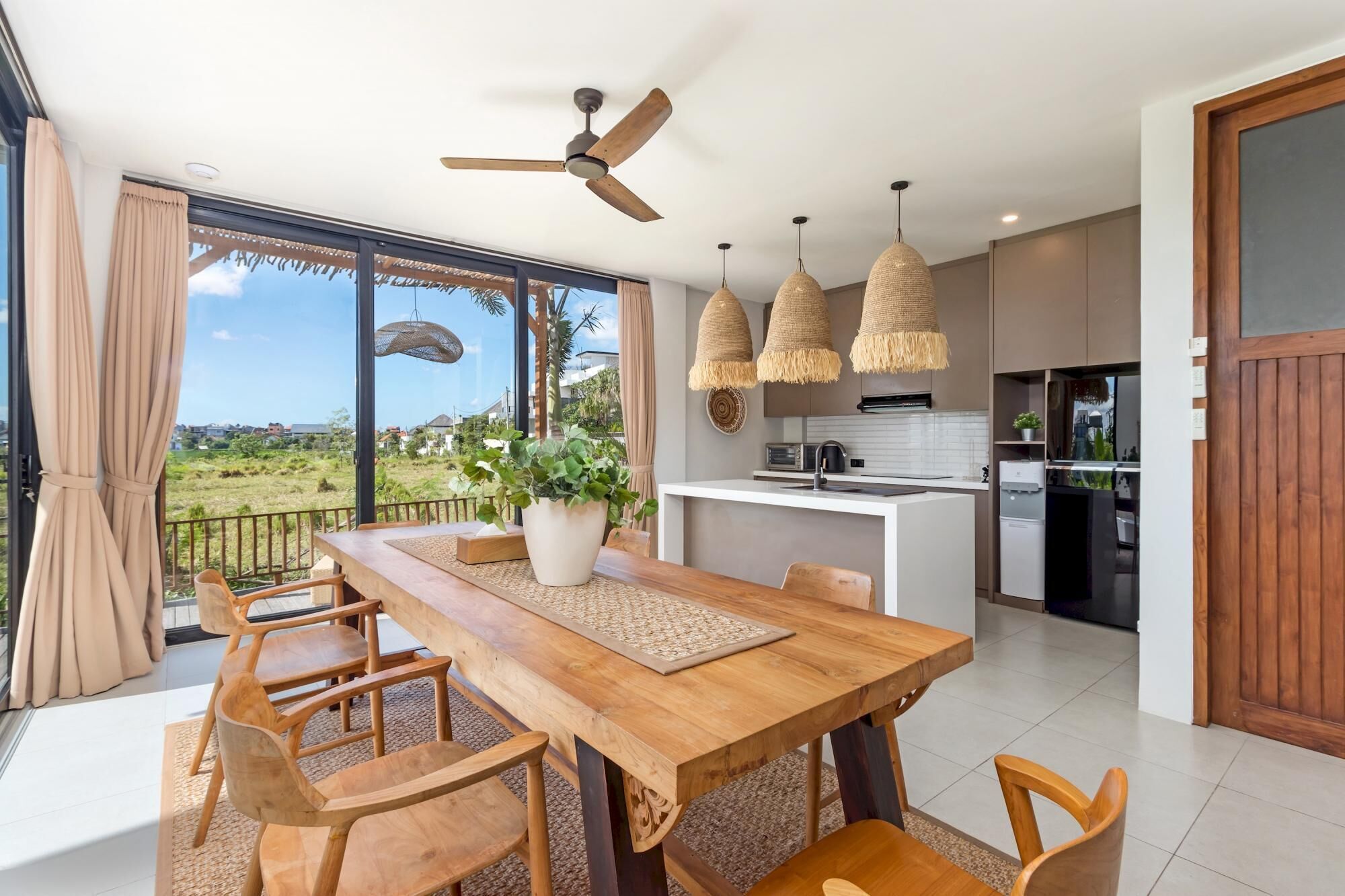 A modern dining area with a wooden table and chairs, a ceiling fan, and a view of the outdoors.