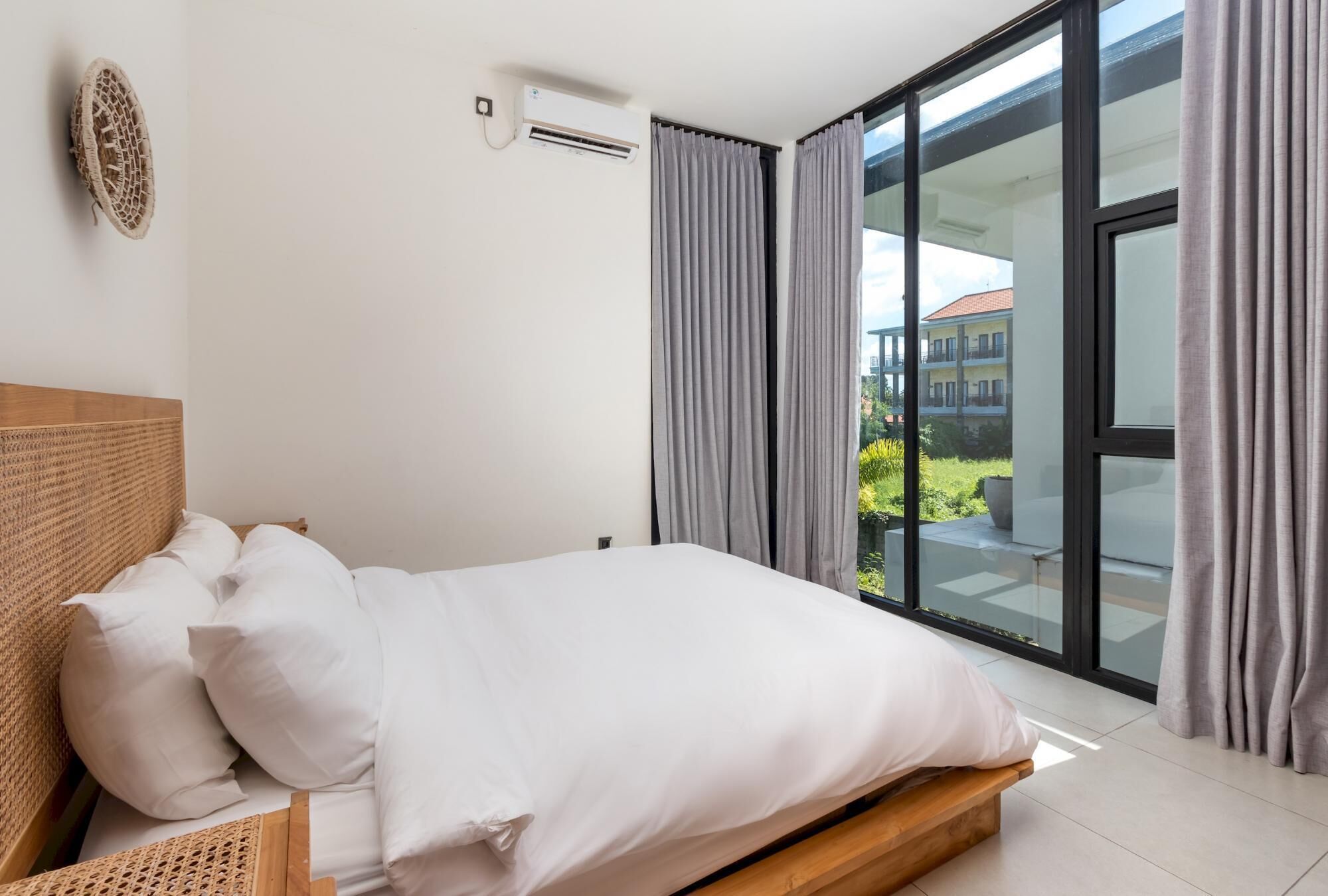 Une chambre moderne avec un lit en bois, du linge de lit blanc et une grande fenêtre avec des rideaux.