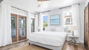Ein Schlafzimmer mit Bett, Deckenventilator, Fenster mit Blick und einer Tür zu einem Außenbereich.