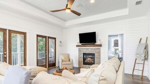 Ein geräumiges Wohnzimmer mit Kamin, Fernseher und Deckenventilator.