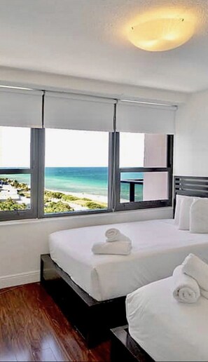 A hotel room with a bed, a view of the beach, and a window with a view of the ocean.