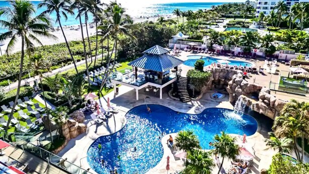 Ein Resort mit mehreren Swimmingpools, Palmen und Blick auf den Strand.