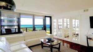 Ein modernes Wohnzimmer mit einem weißen Sofa, einem Glastisch und großen Fenstern mit Blick aufs Meer.