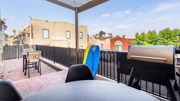 Un patio exterior con una parrilla, sillas y una tabla de surf.