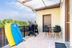 A patio area with a barbecue grill, a table with chairs, and a surfboard leaning against the wall. - 1940's Capitola Village Rental - steps from beach (Capitola)