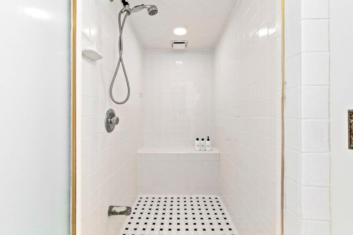 Een kleine badkamer met witte tegels, een handdouche en een kraan op de muur.
