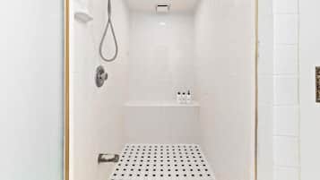 Een kleine badkamer met witte tegels, een handdouche en een kraan op de muur.