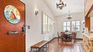 A spacious kitchen with a dining area, large windows, and a wooden door with a sailboat artwork.