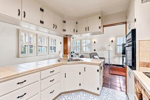 Une cuisine moderne avec des meubles blancs, un four encastré et une grande fenêtre.