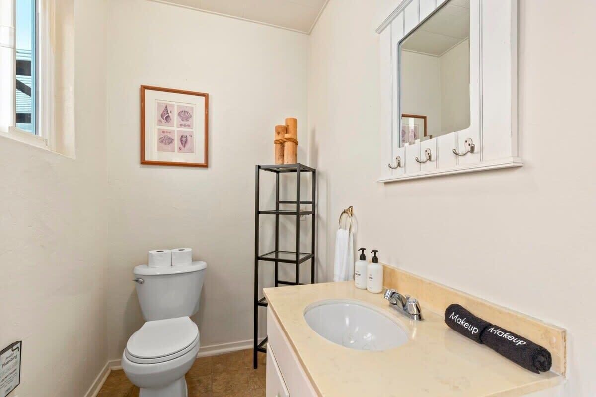 A bathroom with a toilet, sink, mirror, framed artwork, and a black shelf with towels.