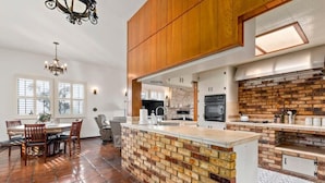 A spacious kitchen with a brick island, wooden cabinets, and a dining area with a chandelier.