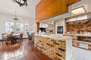 A spacious kitchen with a brick island, wooden cabinets, and a dining area with a chandelier.