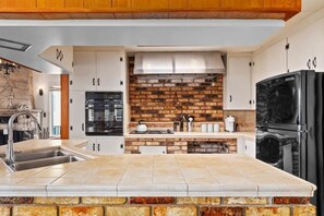 A modern kitchen with white cabinets, a brick backsplash, and a black refrigerator. - 1940's Capitola Village Rental - steps from beach (Capitola)