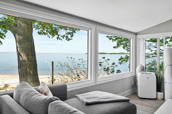 Ein modernes Wohnzimmer mit großen Fenstern, einem grauen Sofa und Meerblick.