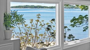 A room with a large window overlooking a body of water, a plant on a shelf, and a sofa. - Crystal Beach Waterfront Cottage - Sunset Views! (Fort Erie)