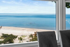 Blick auf einen Strand durch ein Fenster, im Vordergrund ein Stuhl.