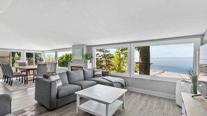 A modern living room with a grey sofa, white coffee table, and large windows overlooking the sea. - Crystal Beach Waterfront Cottage - Sunset Views! (Fort Erie)