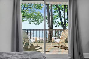 Ein Zimmer mit einer großen Schiebetür zu einem Außenbereich mit einer Holzterrasse, zwei weißen Stühlen und einem Holztisch.