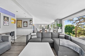 A modern living room with a grey sectional sofa, a white coffee table, and a dining area in the background.