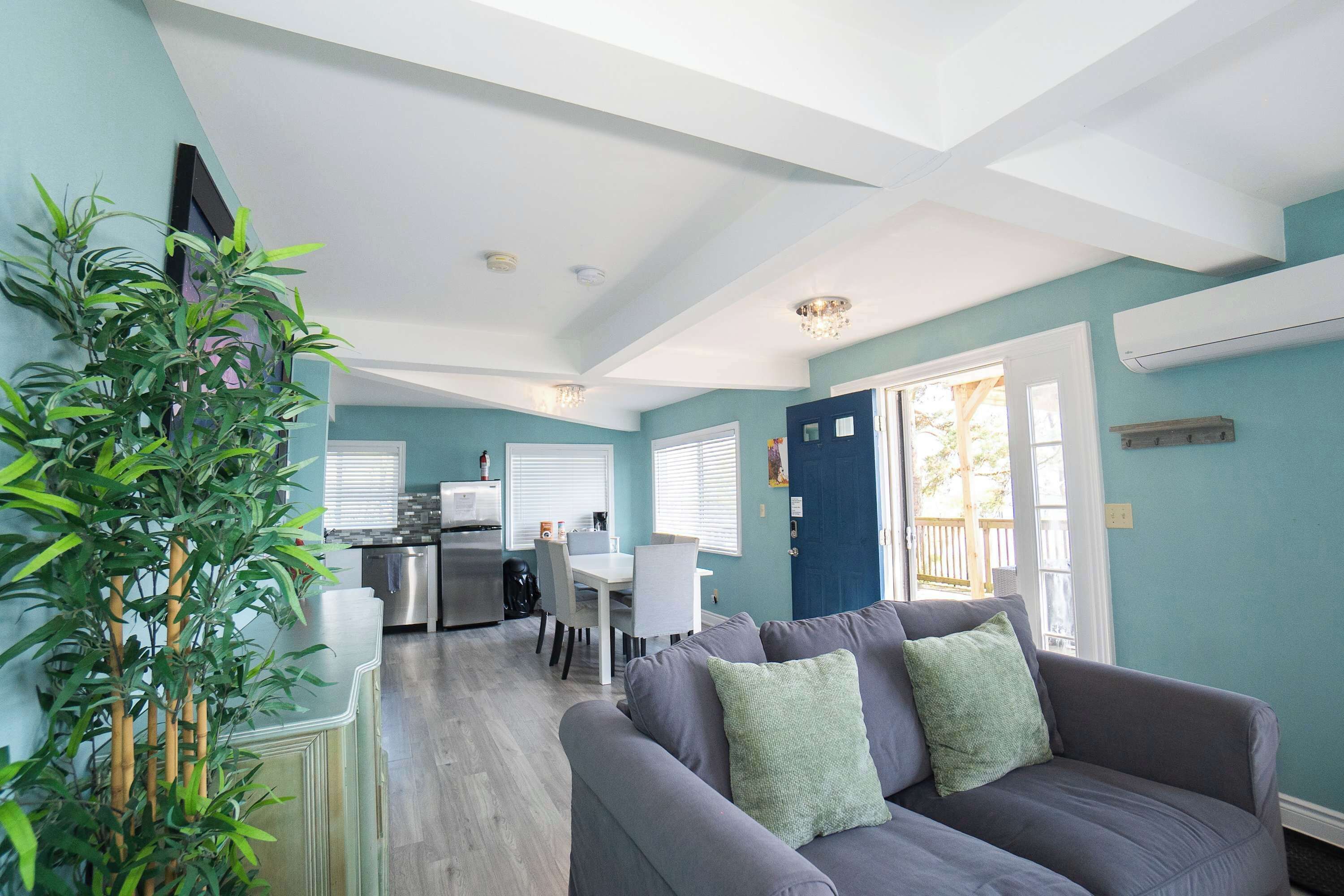 A modern living room with a gray sofa, a dining table, and a kitchen area in the background.