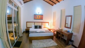 Une chambre d’hôtel comprenant un lit, des tables de chevet, un bureau, une chaise, un miroir et une porte-fenêtre coulissante.