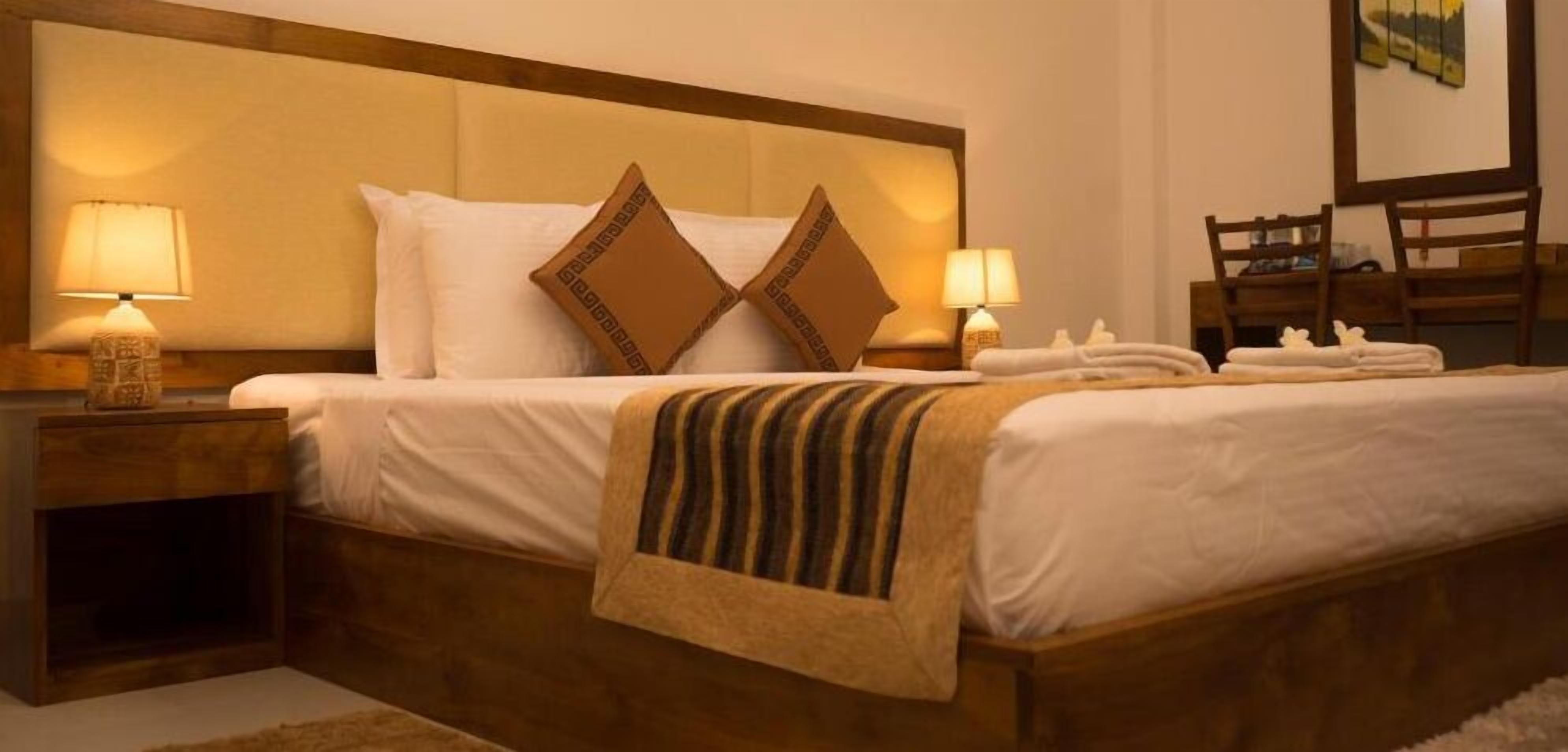 A neatly made bed with white linens, two decorative pillows, and a striped throw blanket. There are two bedside lamps on wooden nightstands.